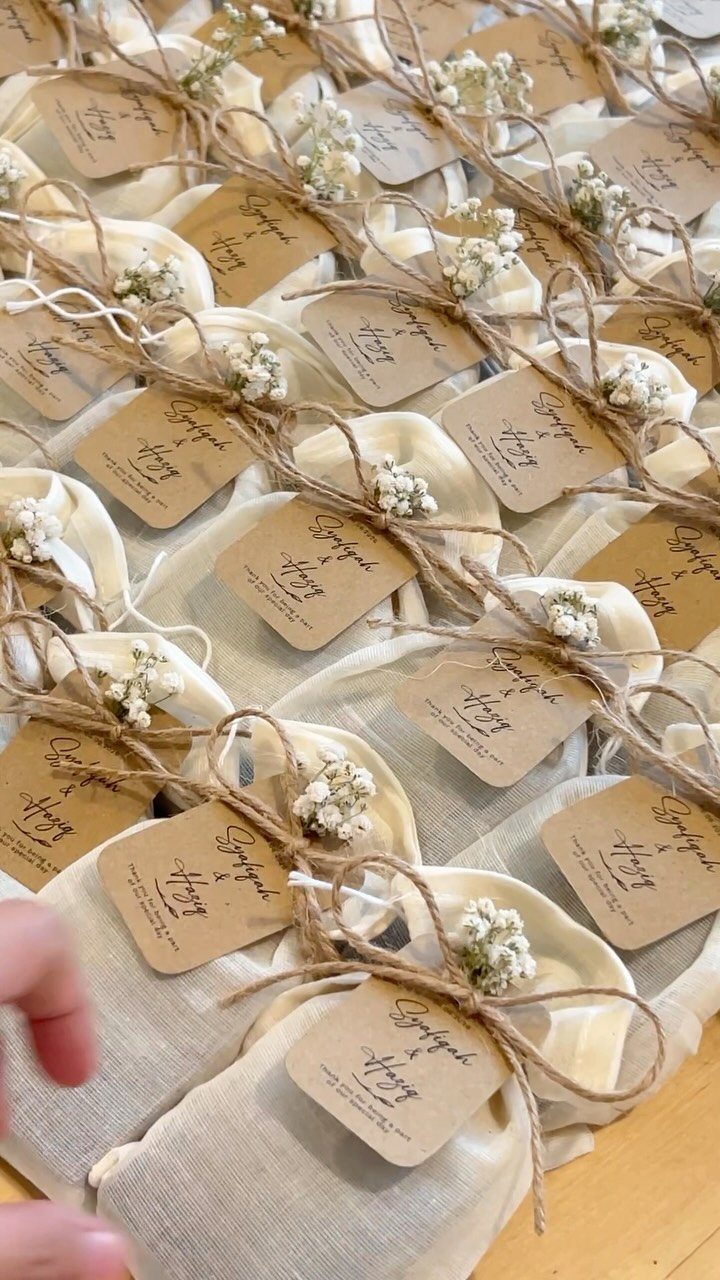 Cream fabric favor pouches tied with twine, baby's breath, and kraft paper tags.