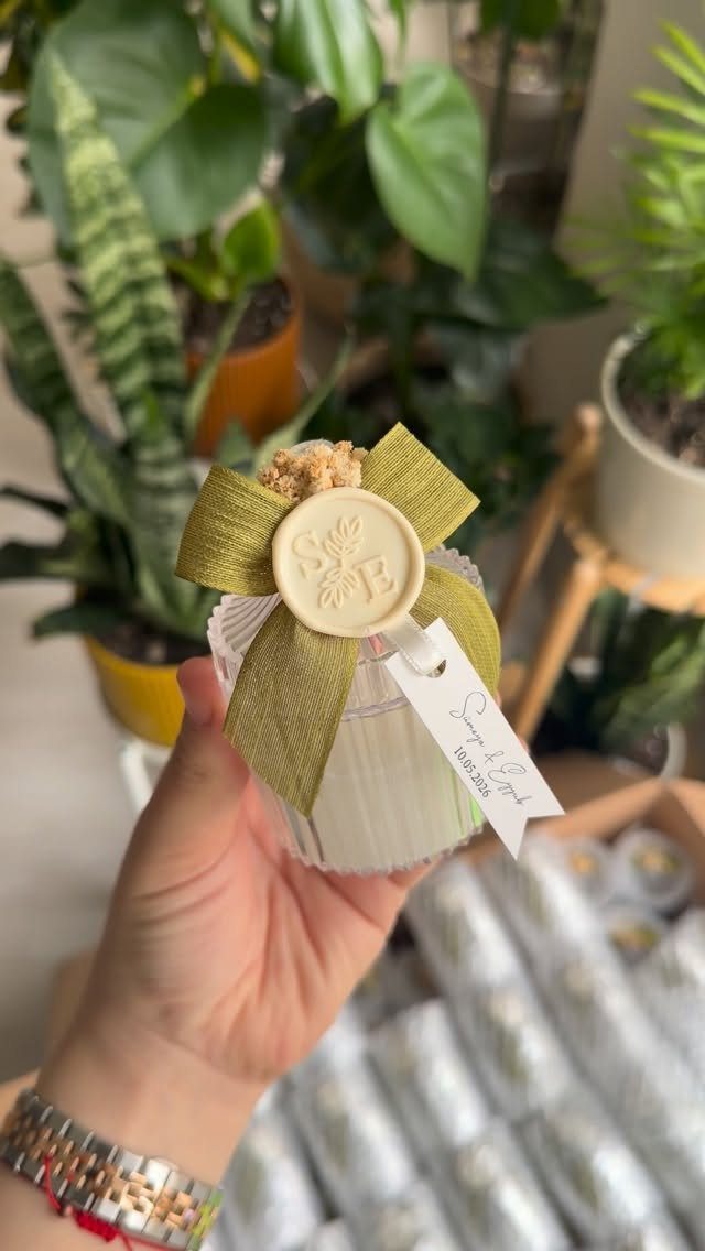 Small white ribbed candle jar with green ribbon and wax seal held by hand