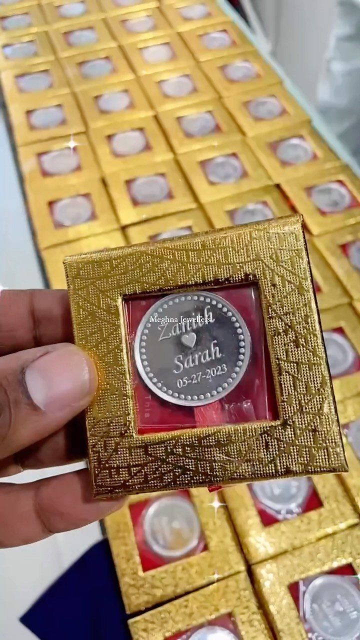 Engraved silver coin in a gold textured gift box held by a hand.