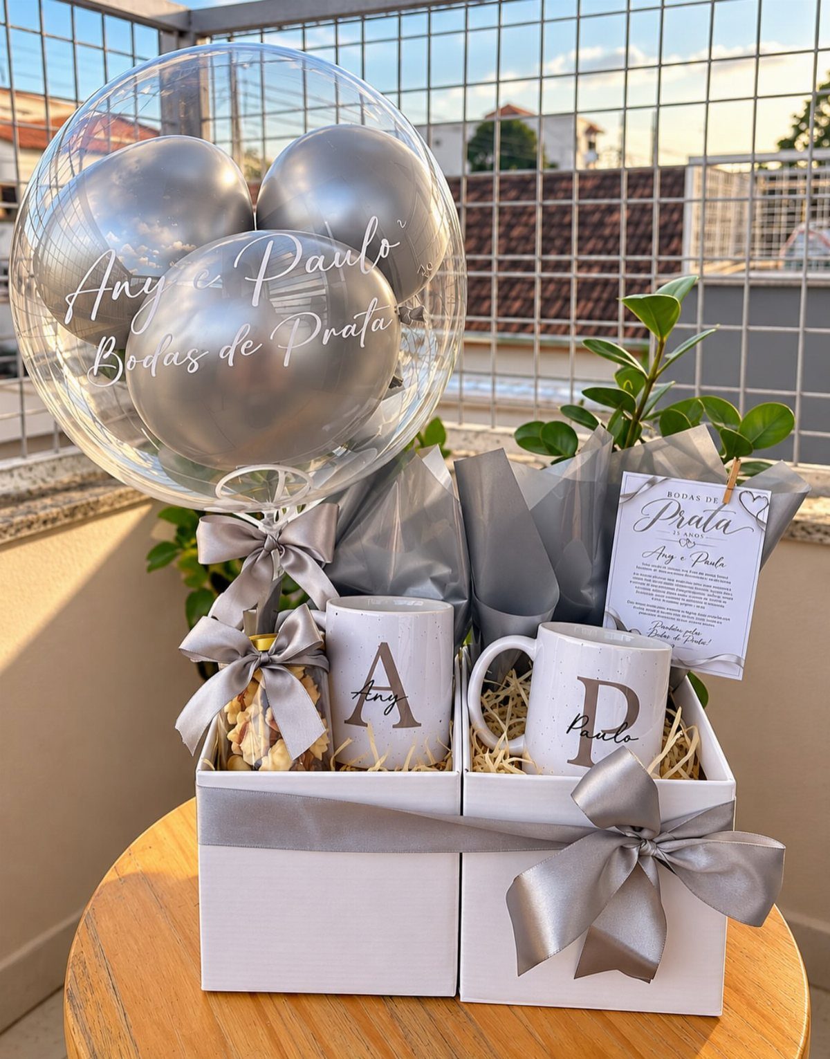 Silver anniversary gift basket with personalized mugs, silver balloons, and ribbons in white boxes.