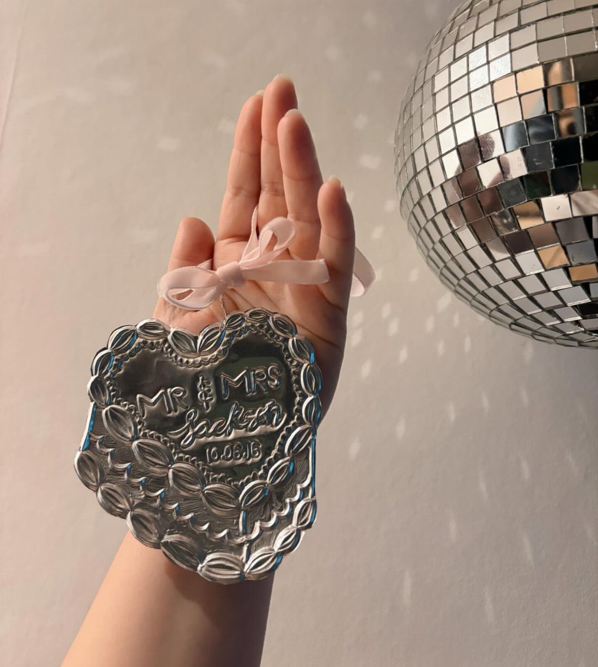Heart-shaped silver anniversary ornament with embossed text held by a hand.