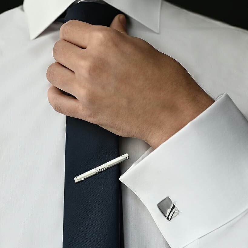 Silver square cufflink on a white dress shirt cuff with a blue tie.