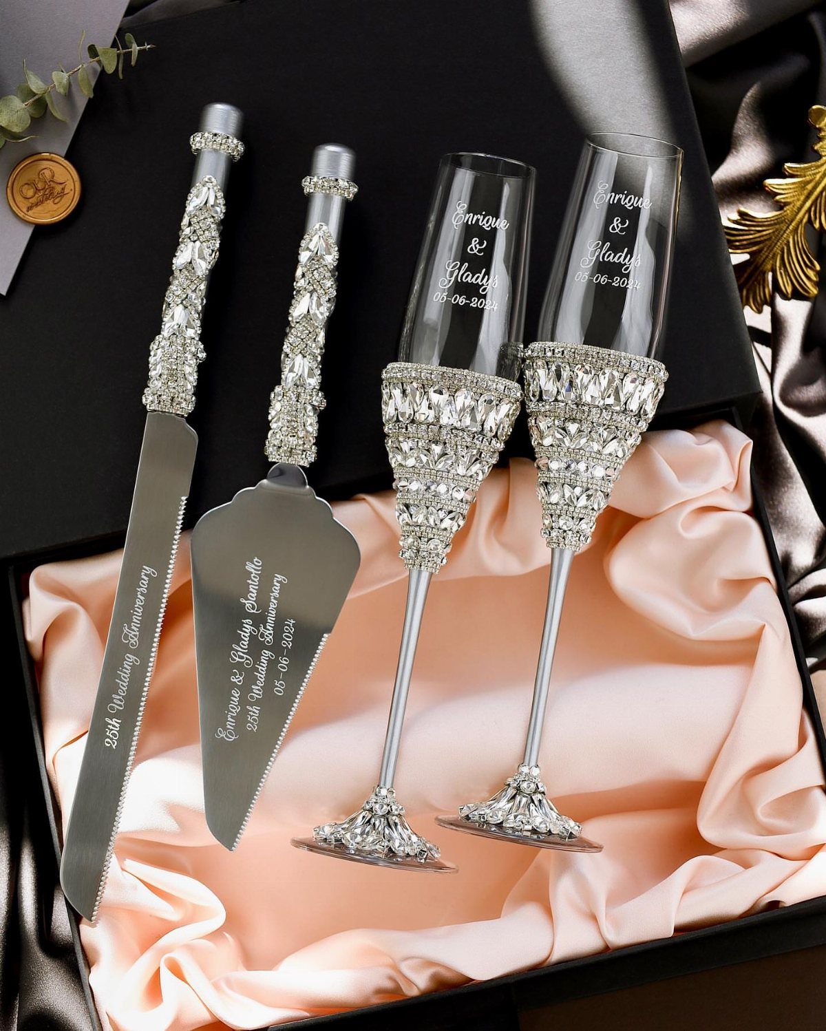 Silver cake server, knife, and champagne flutes with crystals on pink satin.