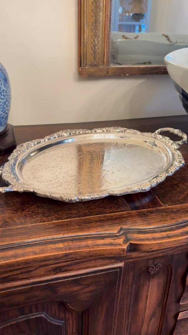 Ornate oval silver serving tray with decorative edges on a dark wooden cabinet