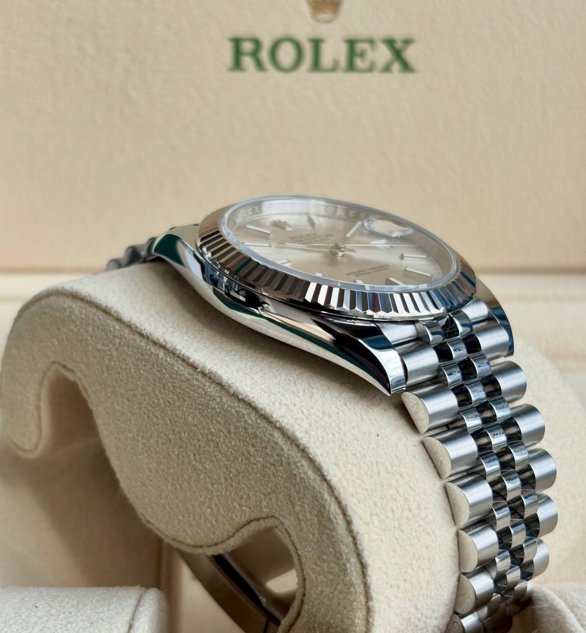 Silver Rolex wristwatch on a beige cushion inside a branded cream box.