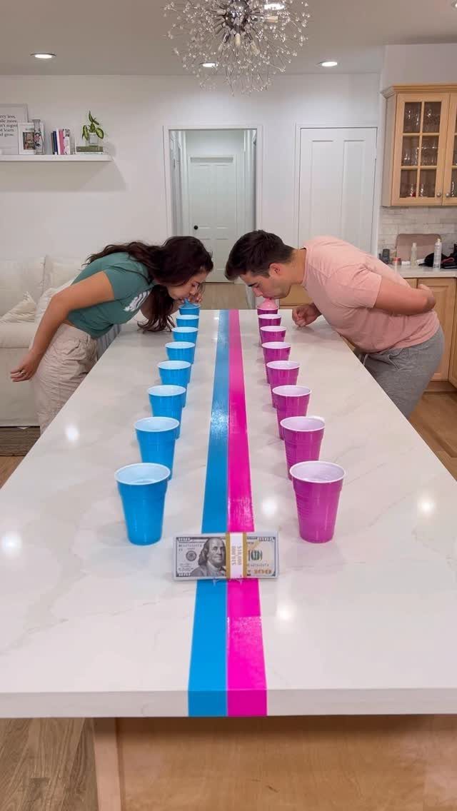Two teenagers competing in a cup game on a white table with colored tape.