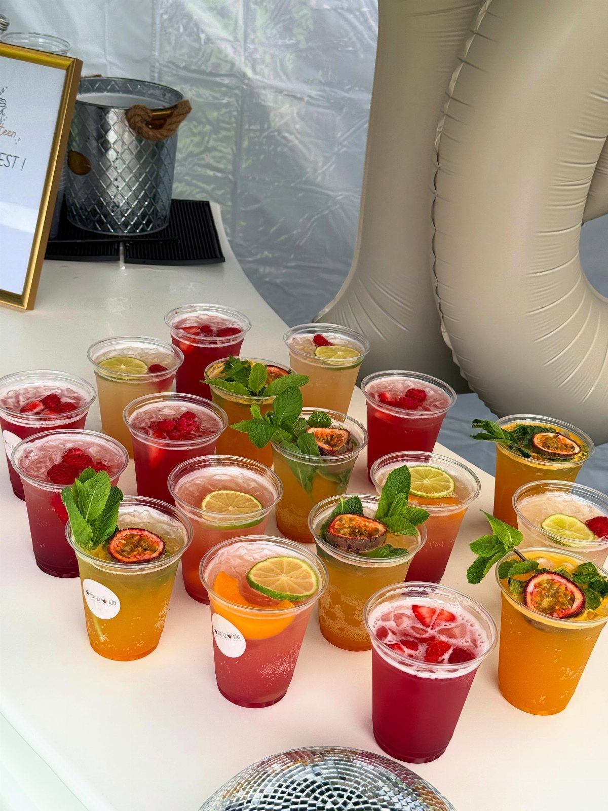 Colorful mocktails with fresh fruit and mint in clear plastic cups on white table