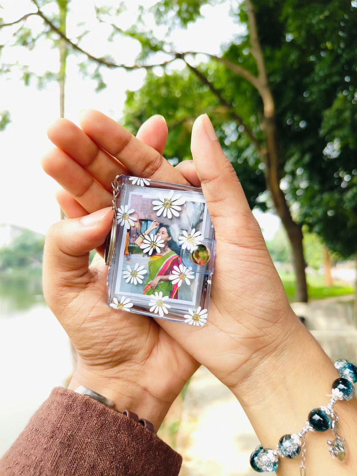 Hands holding a resin block favor with a photo and white daisies.