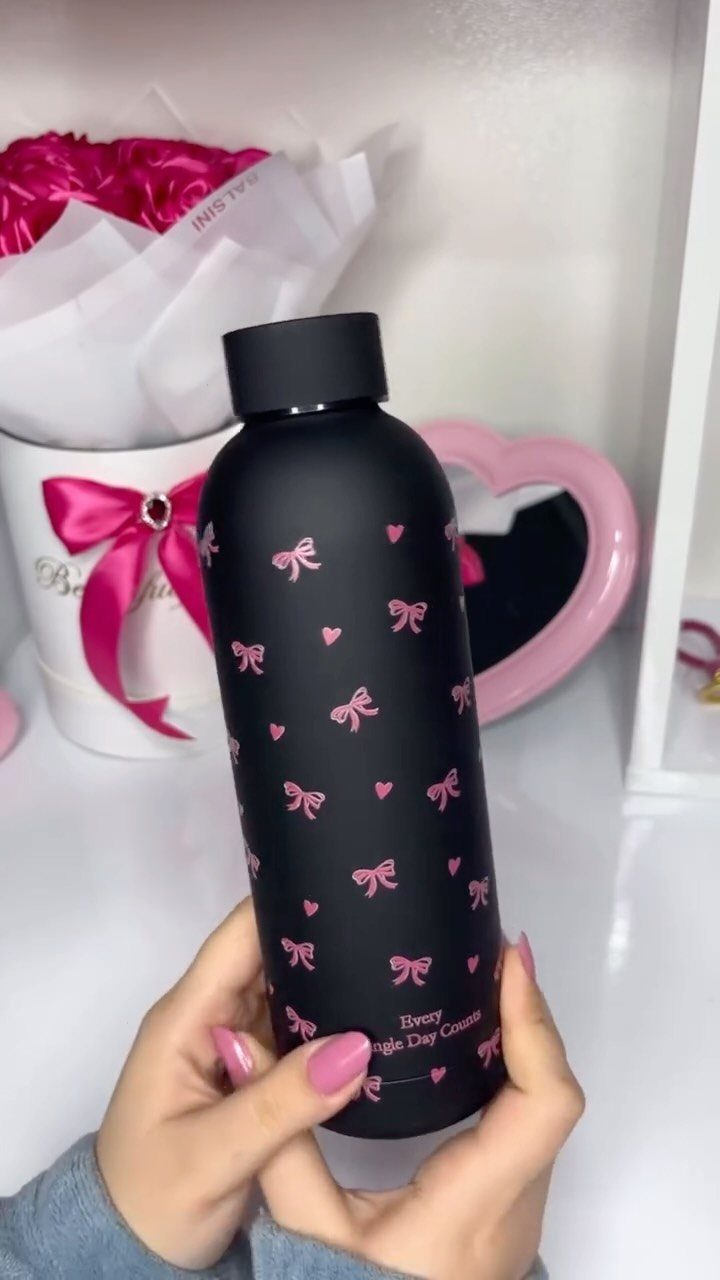 Matte black water bottle with pink bows and hearts held by hands.