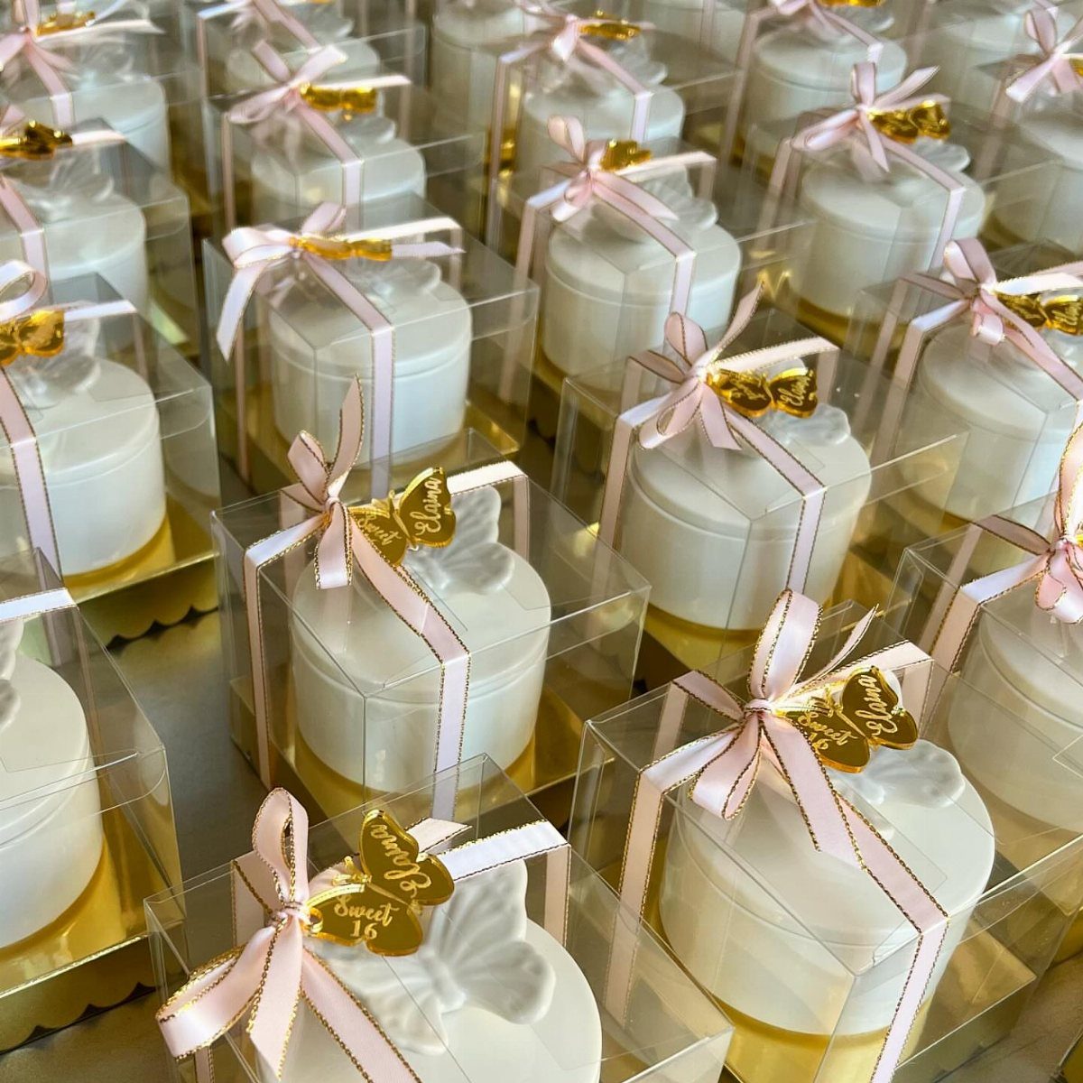 Small white round cakes in clear boxes with pink ribbons and gold butterflies.