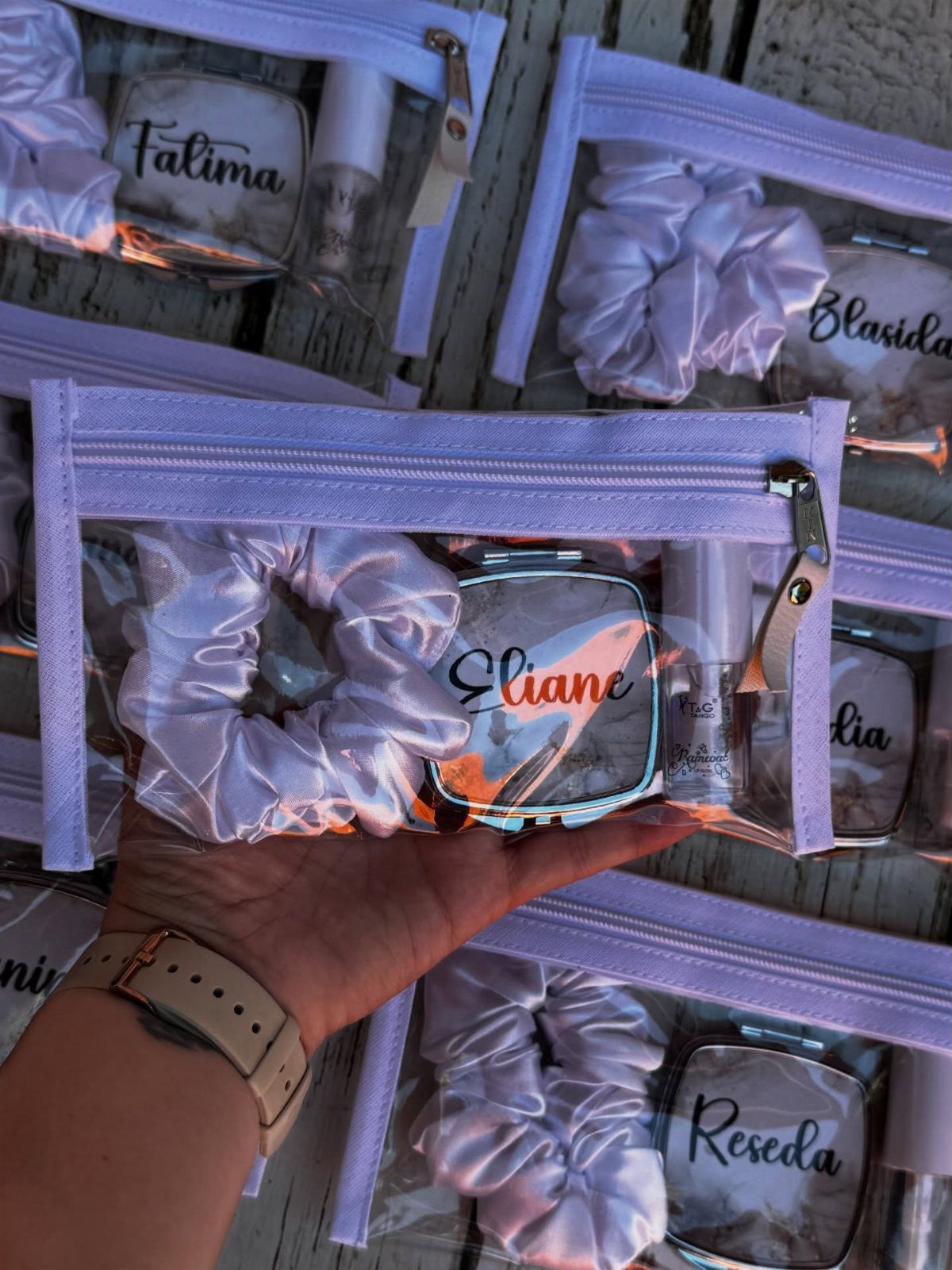 Clear plastic makeup bags with purple zippers containing scrunchies and personalized compact mirrors.