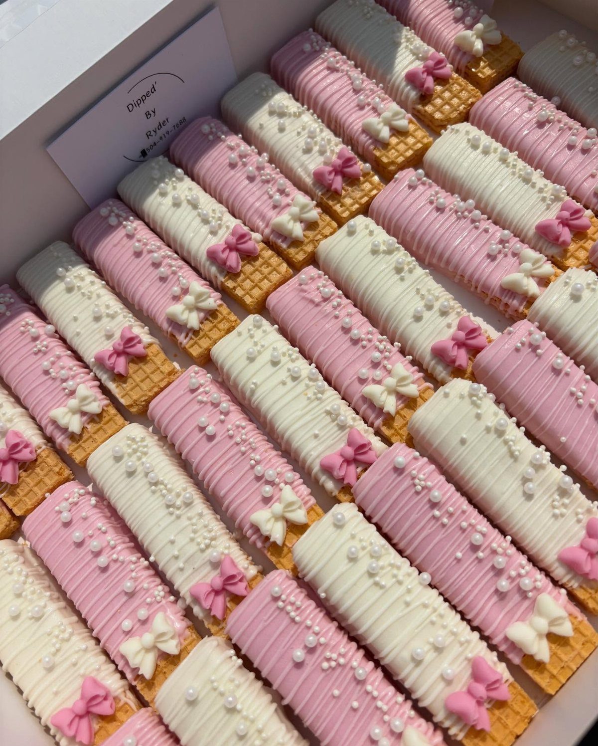 Chocolate covered wafer cookies with pink and white icing, pearls, and tiny bows.