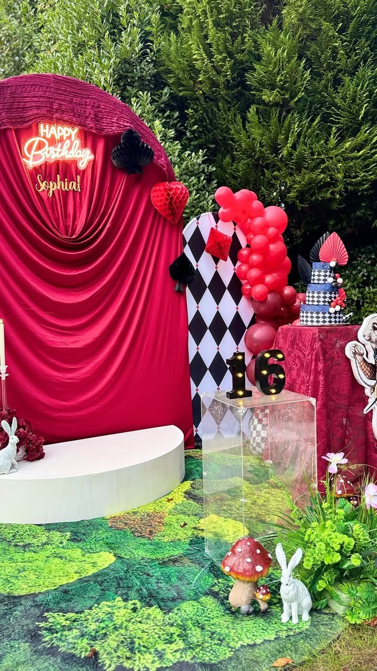Alice in Wonderland party setup with red curtains, checkered wall, and rabbit figurine.