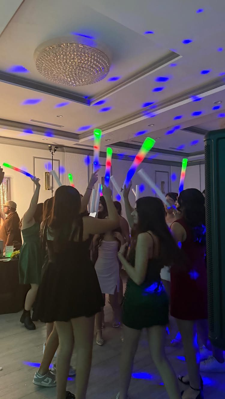 Young women dancing with neon glow sticks under blue disco lights at a party.