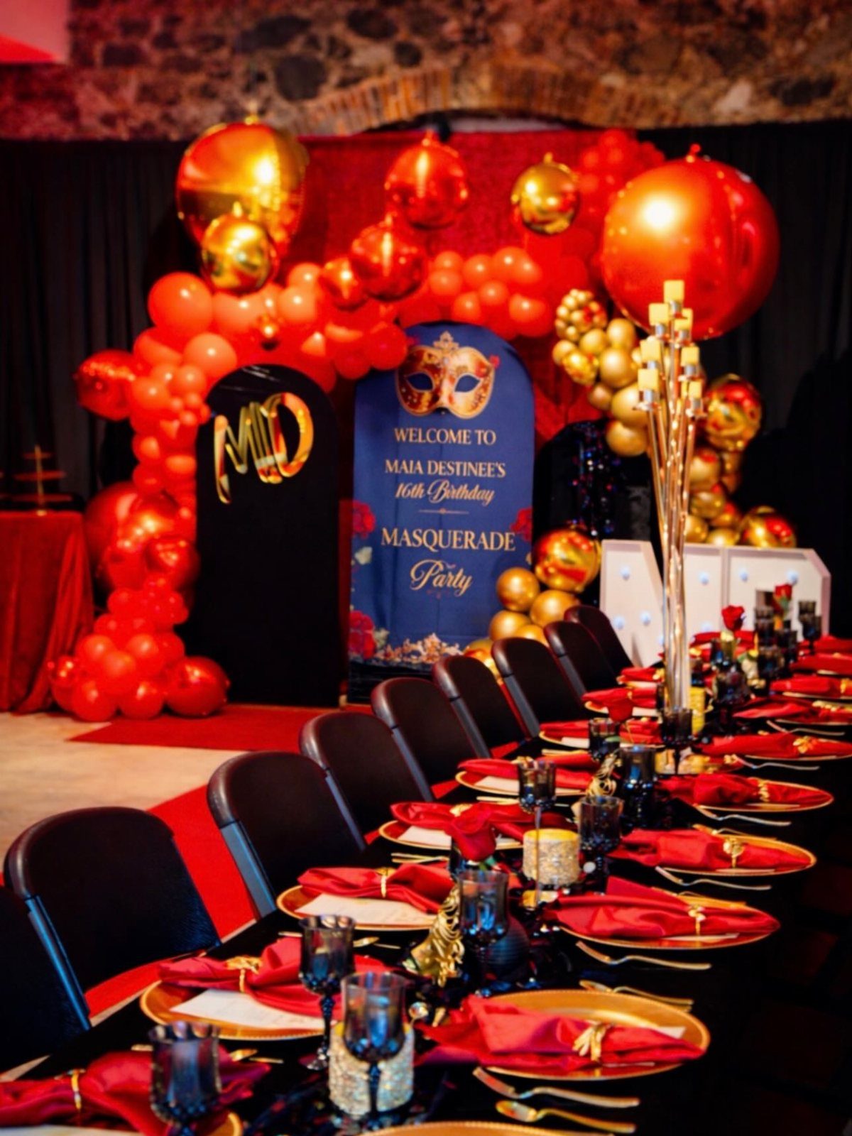 Formal party table setting with red and gold decorations and a masquerade banner.