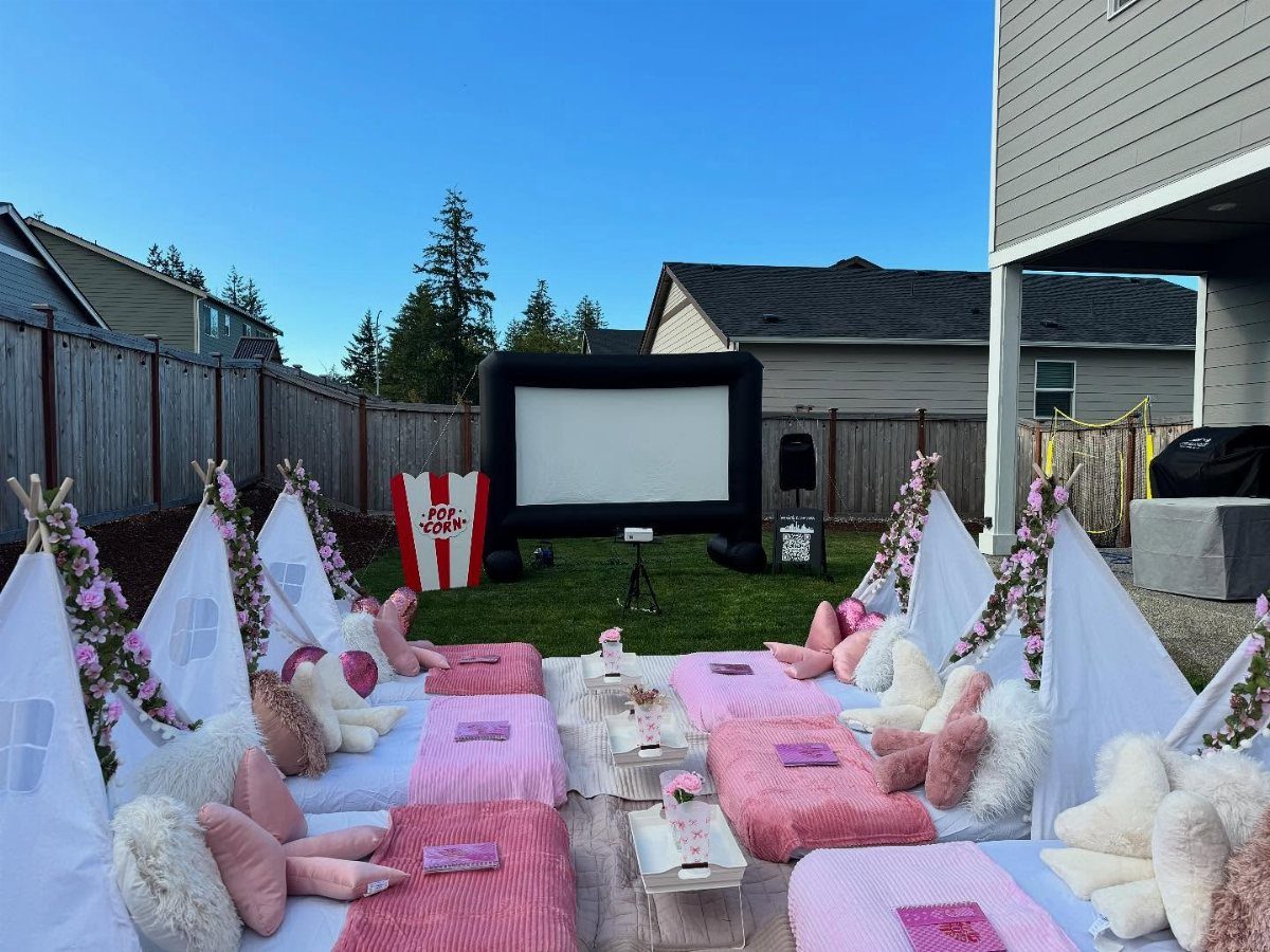 Outdoor movie night setup with inflatable screen, teepees, and pink bedding in backyard
