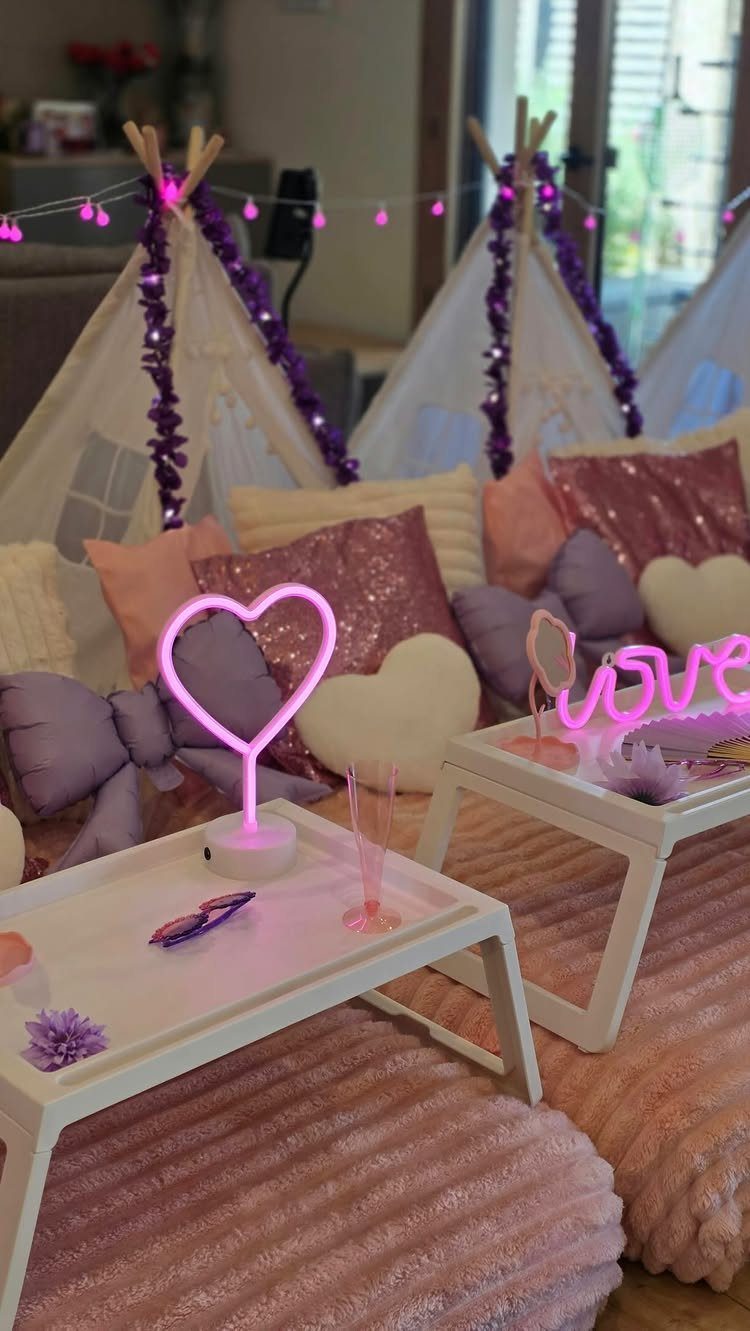 Teepee tents and plush pillows with pink neon lights for a slumber party.