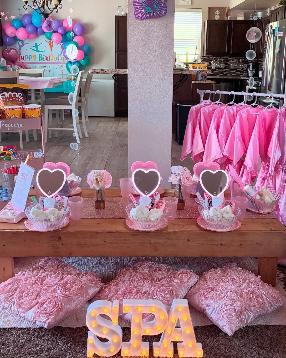 Pink spa party setup with illuminated SPA letters, robes, and heart mirrors.
