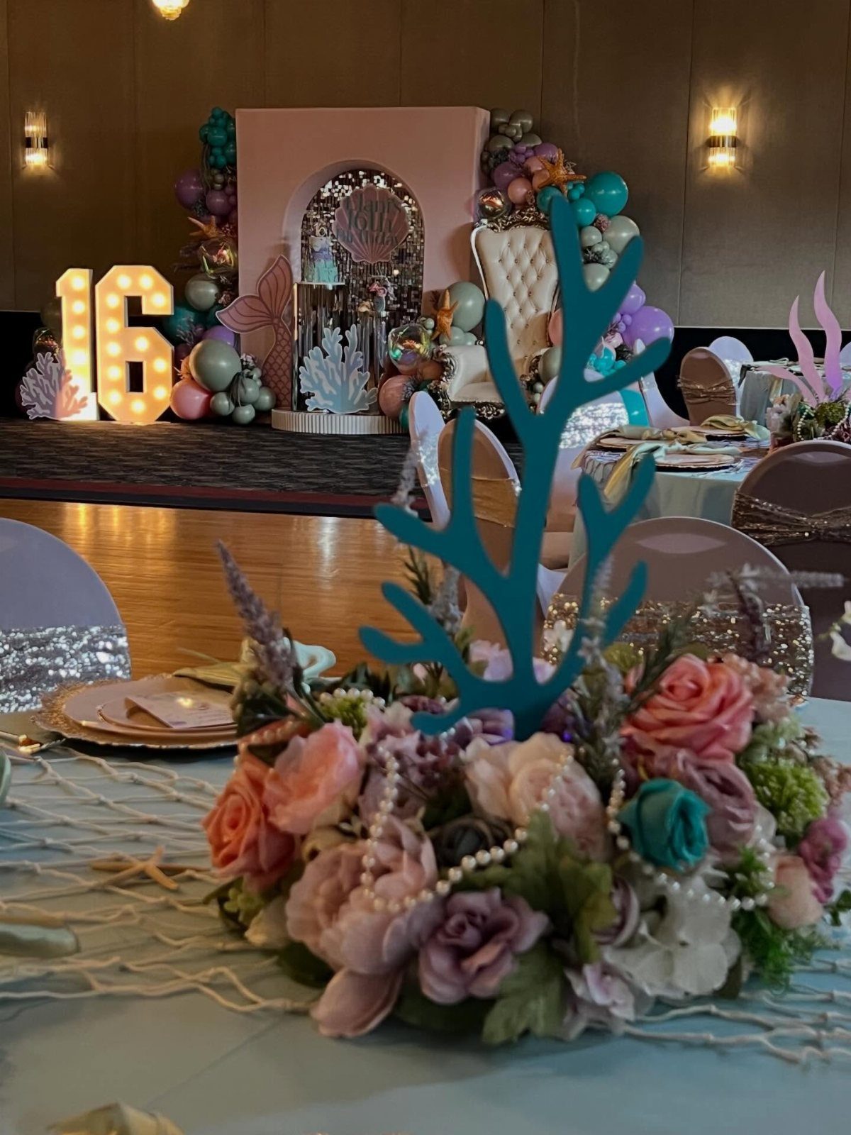 Floral centerpiece with teal coral cutout and light-up 16 sign for ocean party.