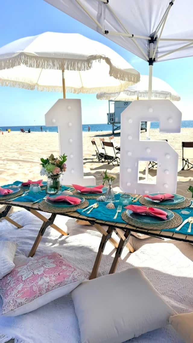 Beach party table setting with large illuminated 16 numbers and white umbrellas.
