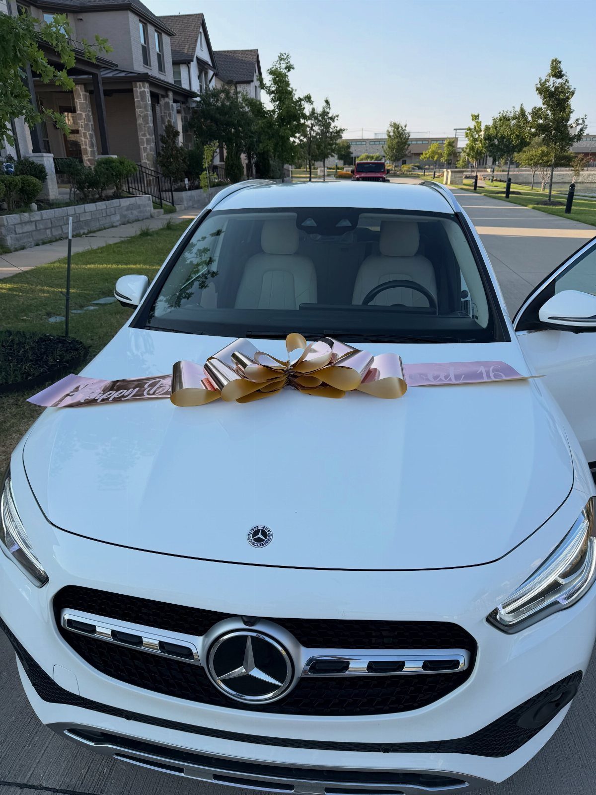 White Mercedes-Benz car with a large rose-gold bow and ribbon on the hood.
