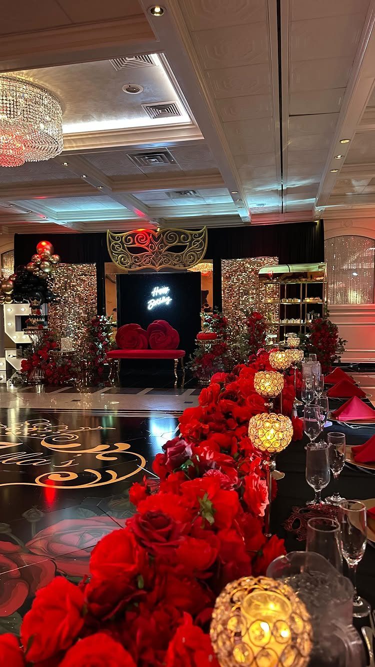 Masquerade party setup with a large gold mask, red roses, and crystal chandeliers.