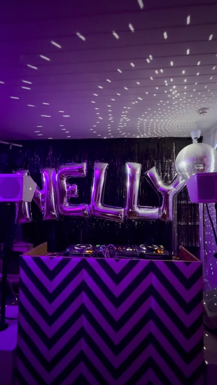 DJ booth with purple chevron pattern and silver NELLY balloons against black tinsel.