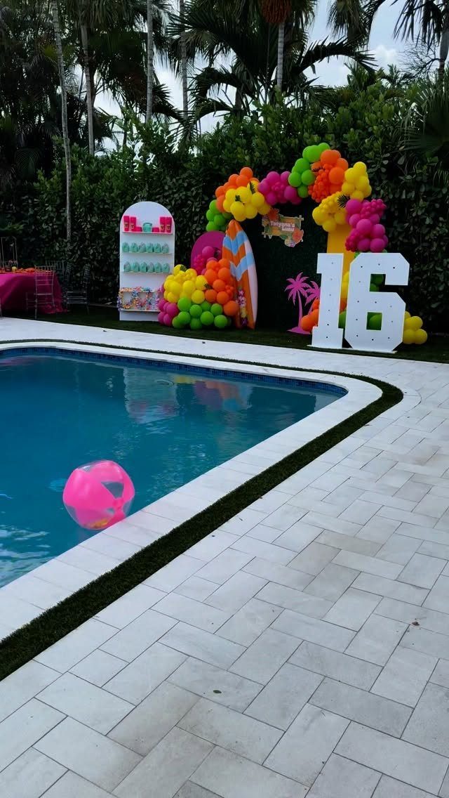Poolside birthday party setup with colorful balloons, a large 16 sign, and palm trees.