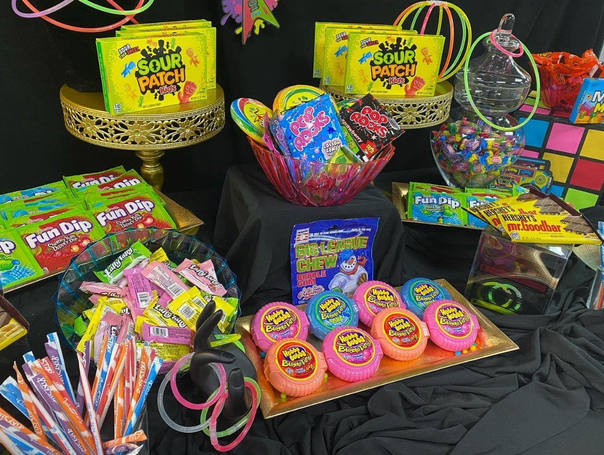 Neon candy table with 80s treats, glow sticks, and a Rubik's Cube.