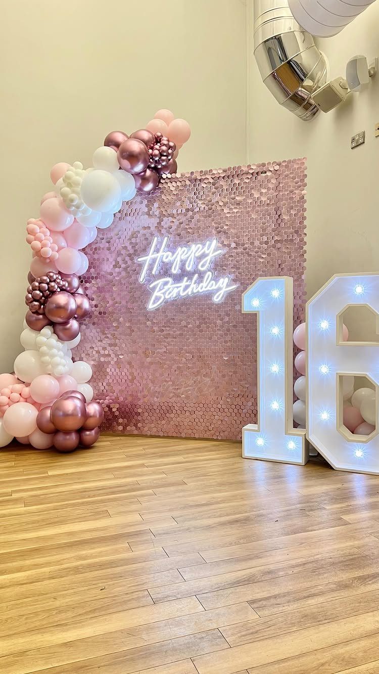 Pink and white balloon garland framing a sequin backdrop and illuminated number 16.