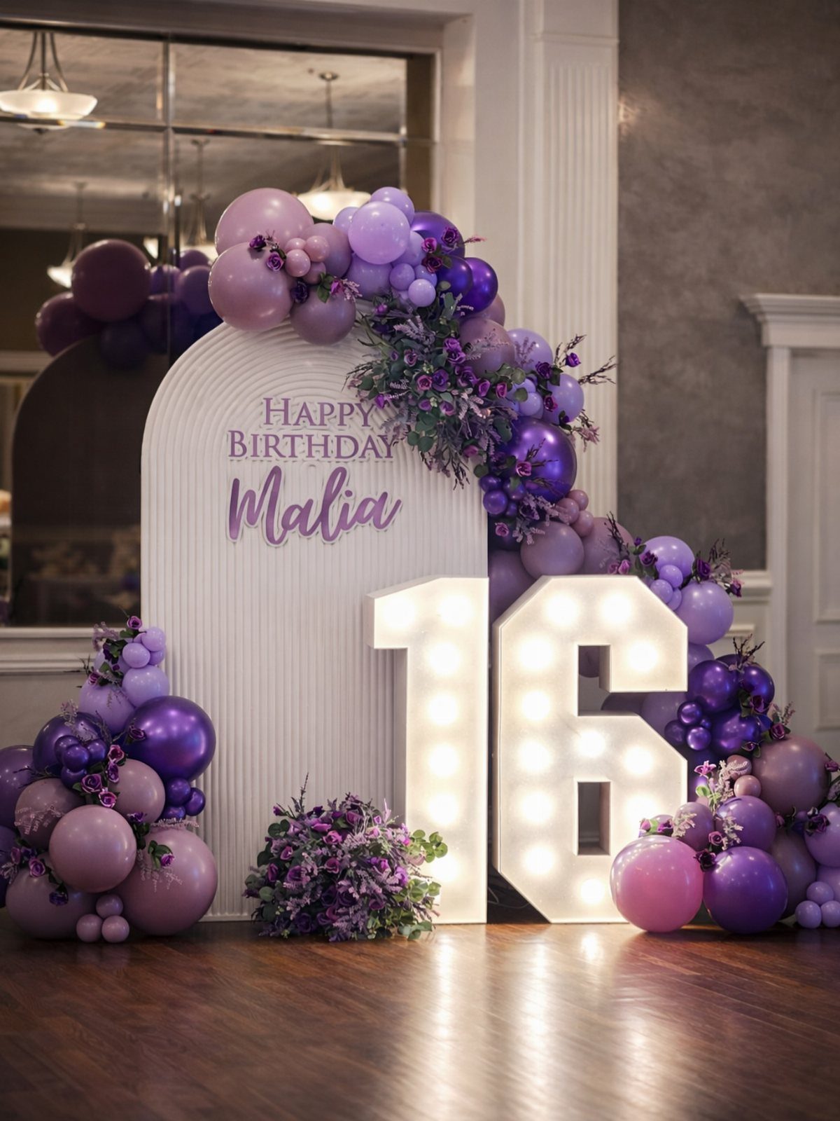 Purple and lavender balloon arch with glowing number 16 marquee lights and backdrop.