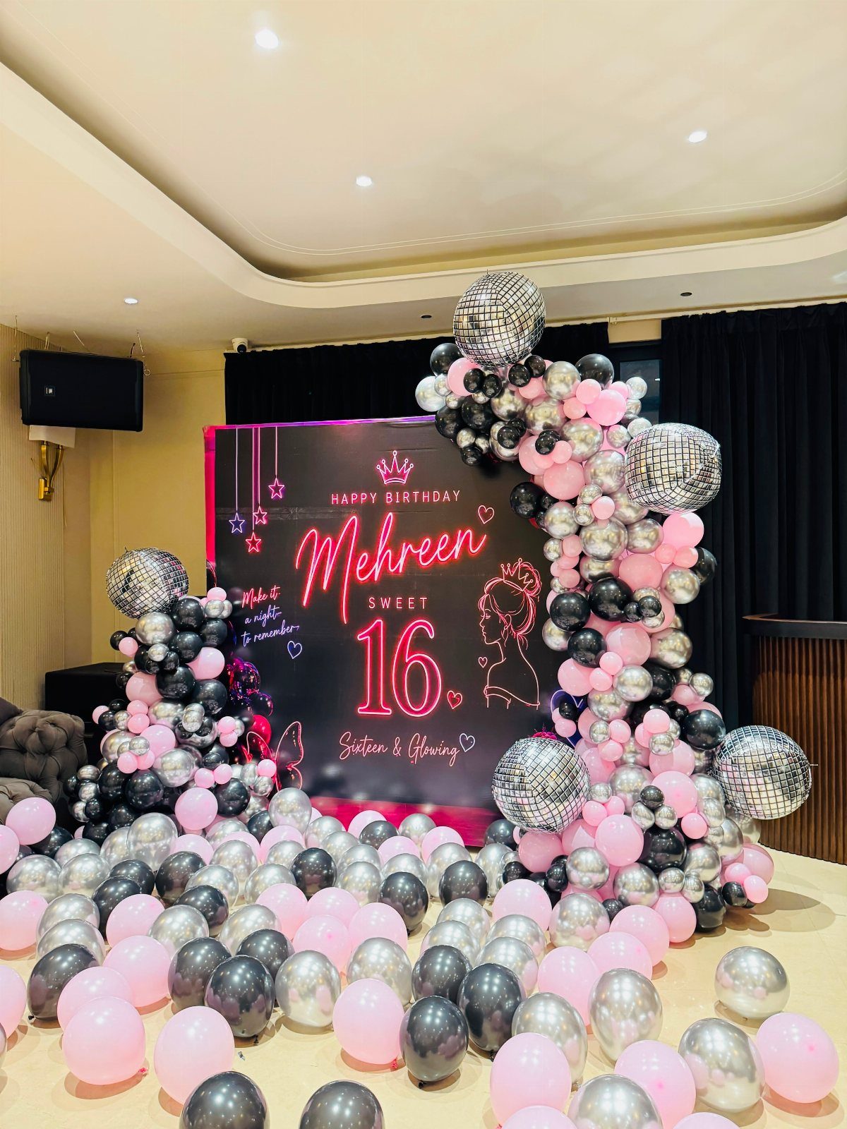Pink neon Sweet 16 sign surrounded by pink and silver balloons and disco balls