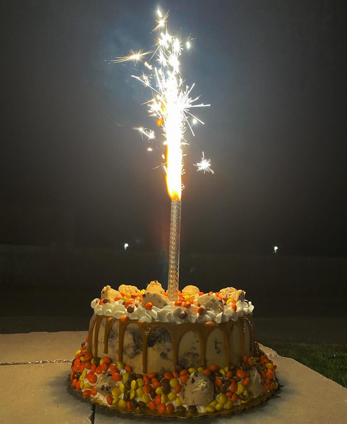 Cake with caramel and candy topped with a lit sparkling candle at night