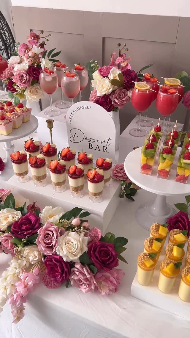 Dessert bar table with pink flowers, fruit parfaits, and pink drinks in glasses.