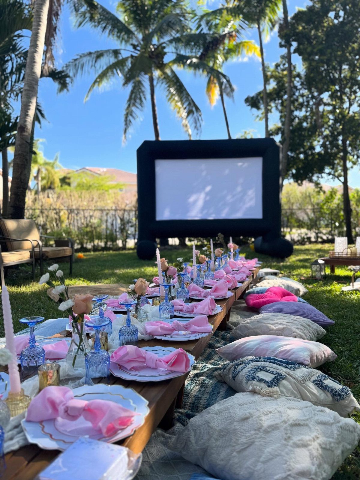 Outdoor movie screen and low dining table with pink accents in a sunny backyard