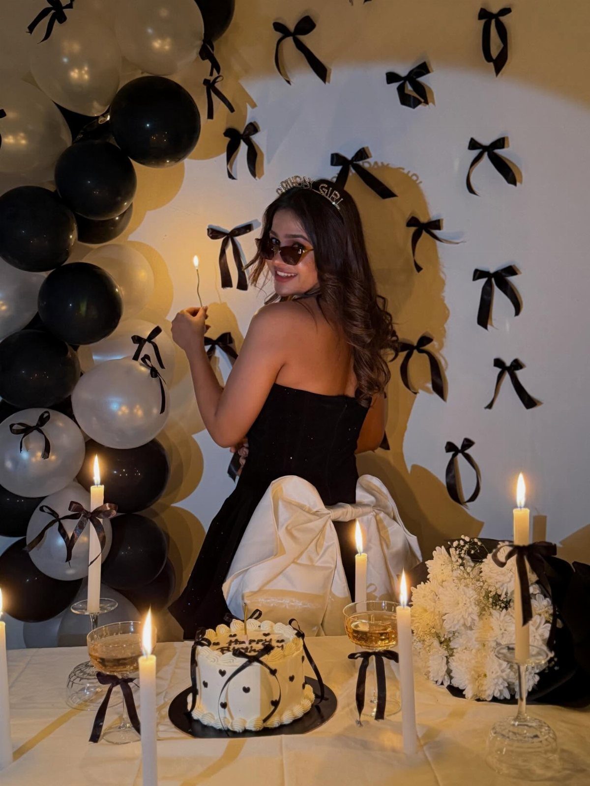 Young woman in black dress posing with black and white balloons and cake.