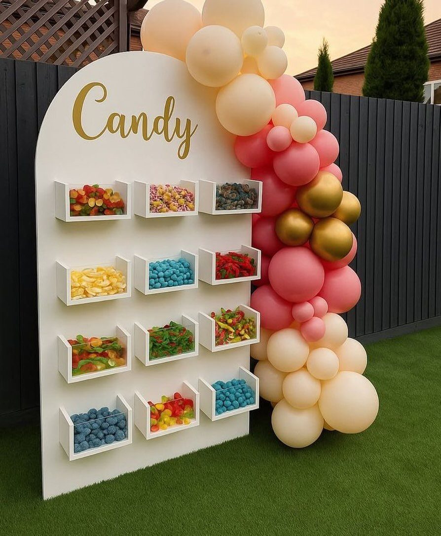 Candy buffet wall with colorful treats and a pink and gold balloon garland.