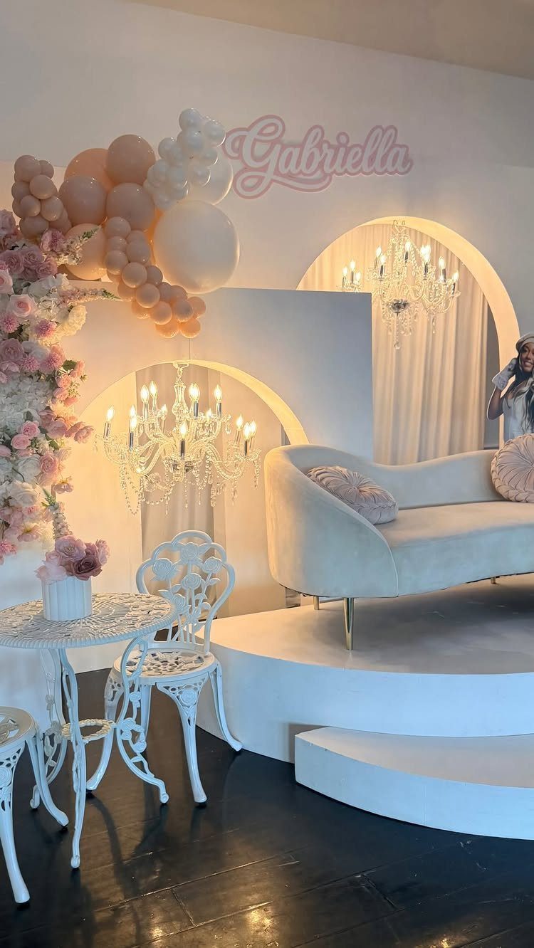 Elegant party setup with white furniture, pink balloons, and crystal chandeliers for Gabriella.