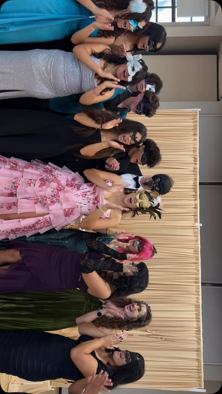 Group of teenagers in formal wear and masquerade masks posing against a curtain.