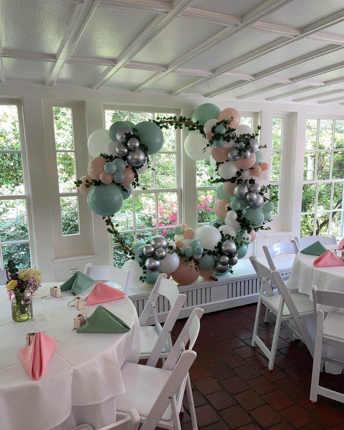Crescent-shaped balloon arch in mint, silver, and pink in a white sunroom.