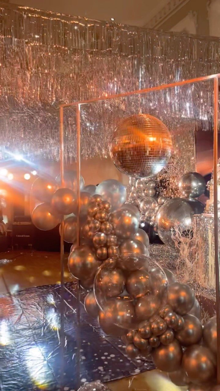 Mirrored disco ball and metallic balloons in front of silver tinsel party backdrop