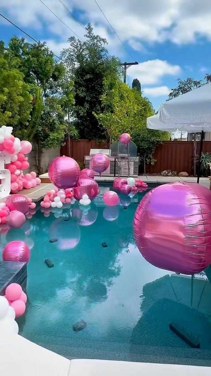 Swimming pool decorated with floating pink and white balloons for a party.