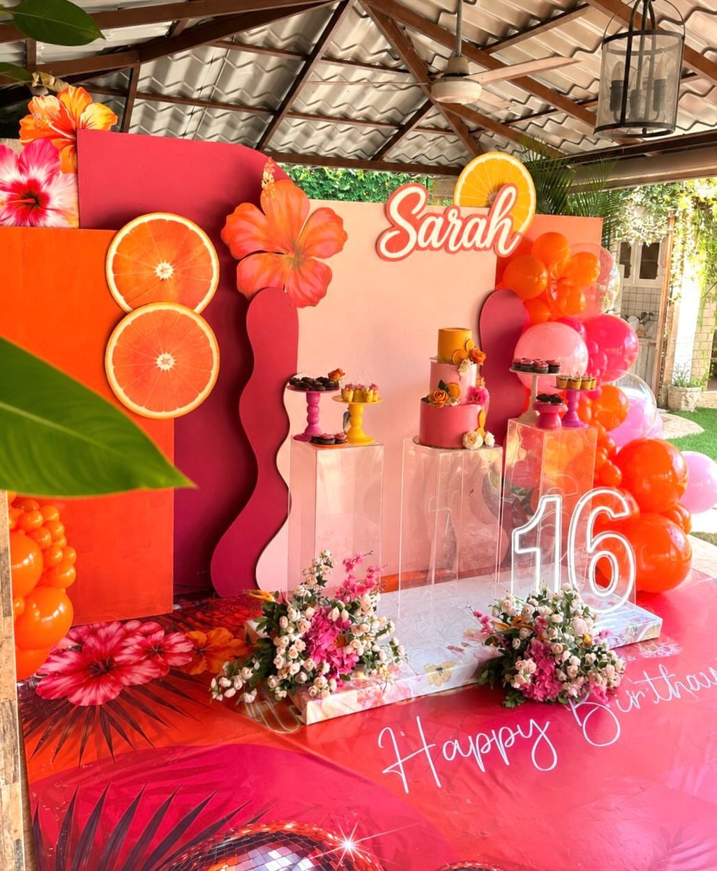 Tropical birthday dessert table with orange and pink decorations and a number 16 sign