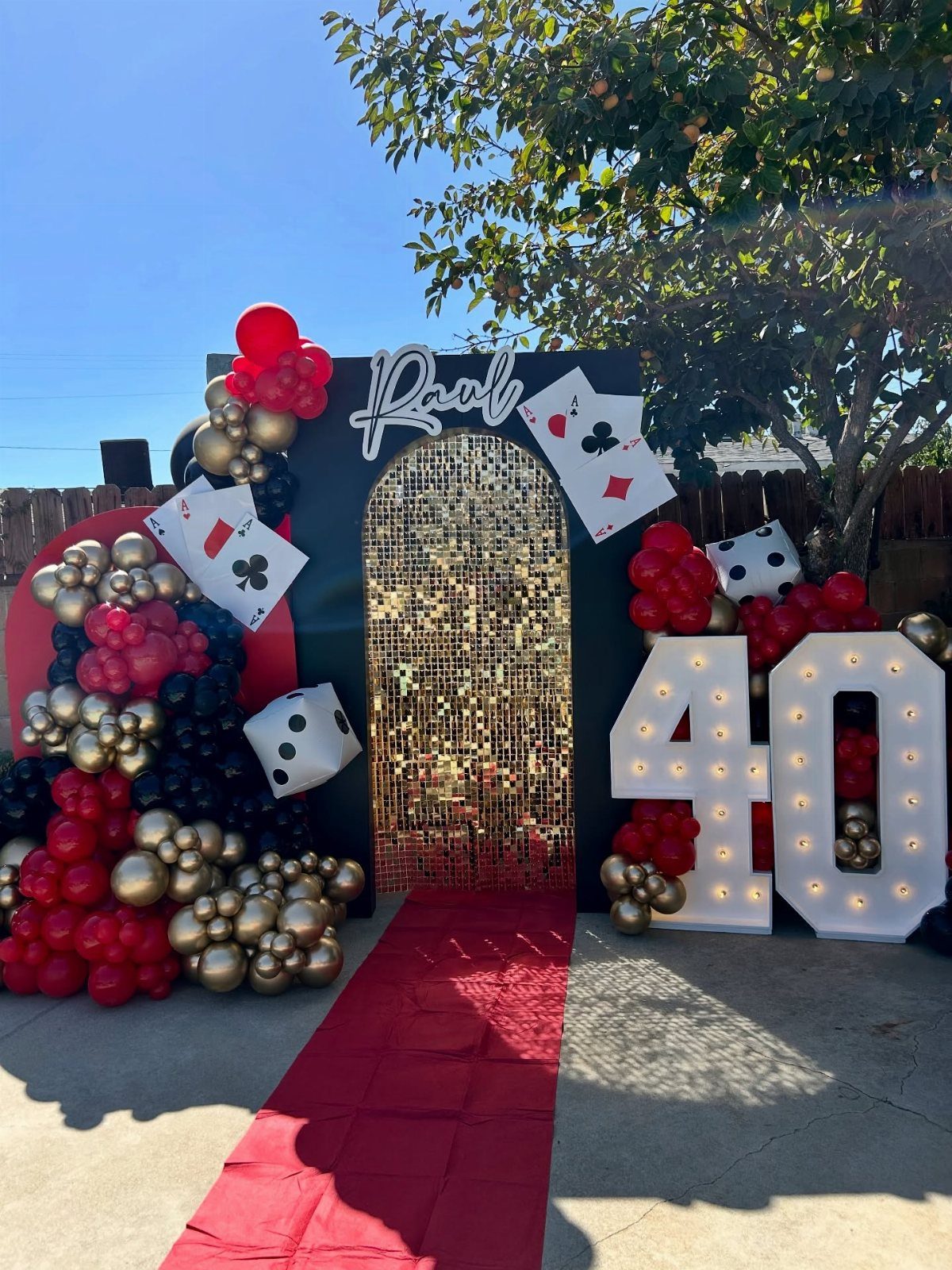 Birthday party setup with red carpet, gold backdrop, balloons, and casino-themed decorations.