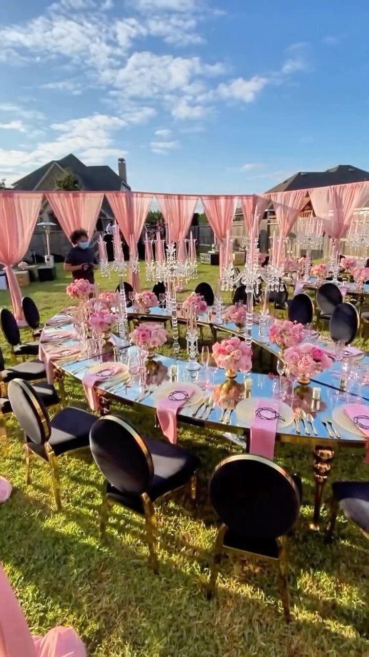 Mirrored table with pink flowers and black chairs under pink fabric canopies outdoors.