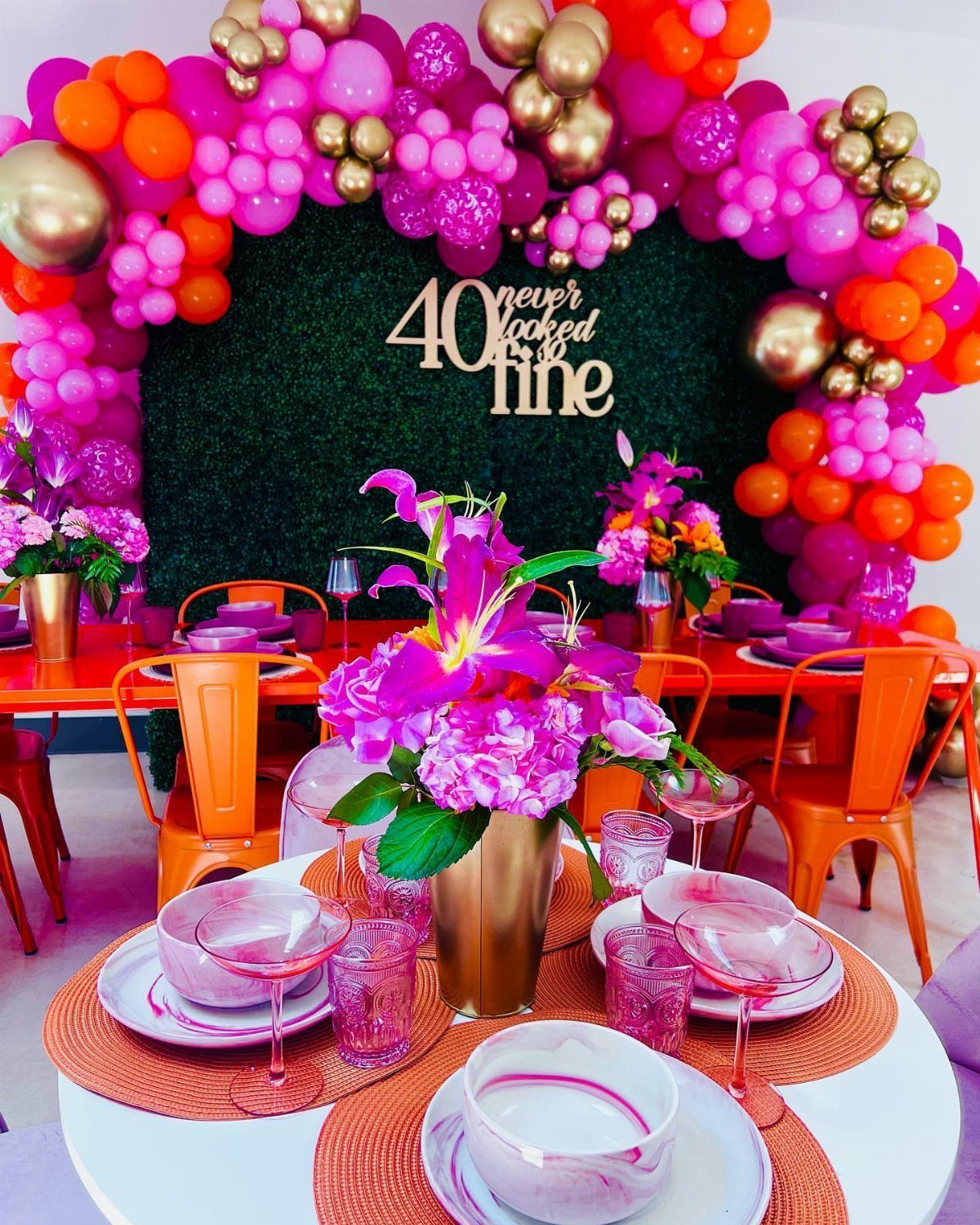 Festive 40th birthday party setup with pink balloon arch and orange table settings.