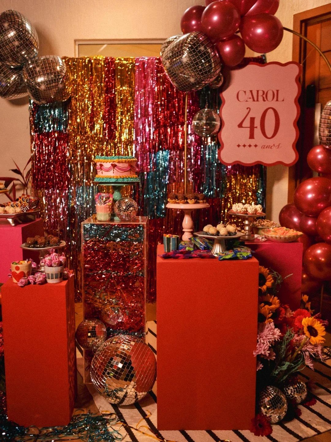 Disco ball decorations and red pedestals with treats for a 40th birthday party.