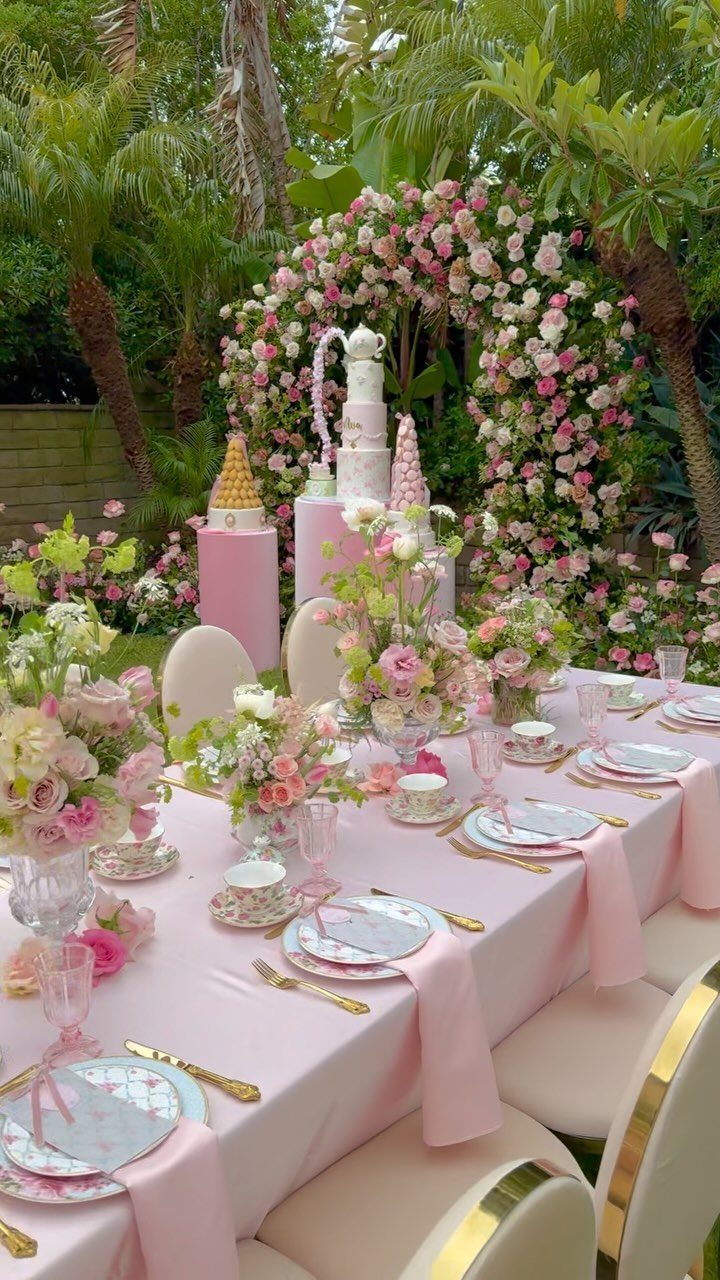 Elegant garden tea party setup with pink linens, floral arrangements, and teapot cake.