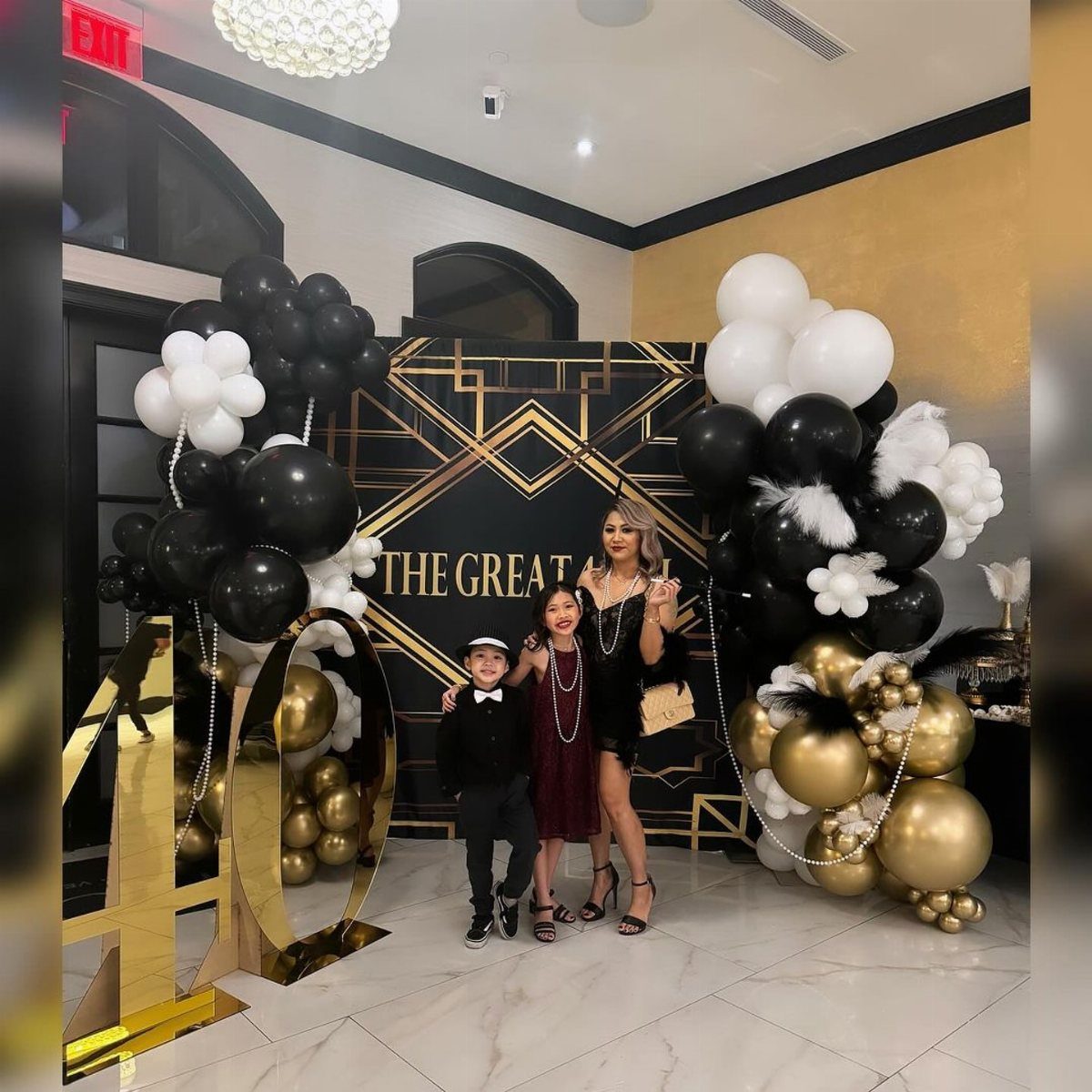 Three people posing by a gold and black Gatsby themed 40th birthday backdrop.