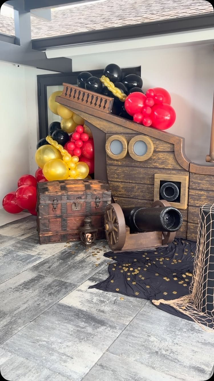 Pirate party decor with a wooden ship, cannon, treasure chest, and colorful balloons.